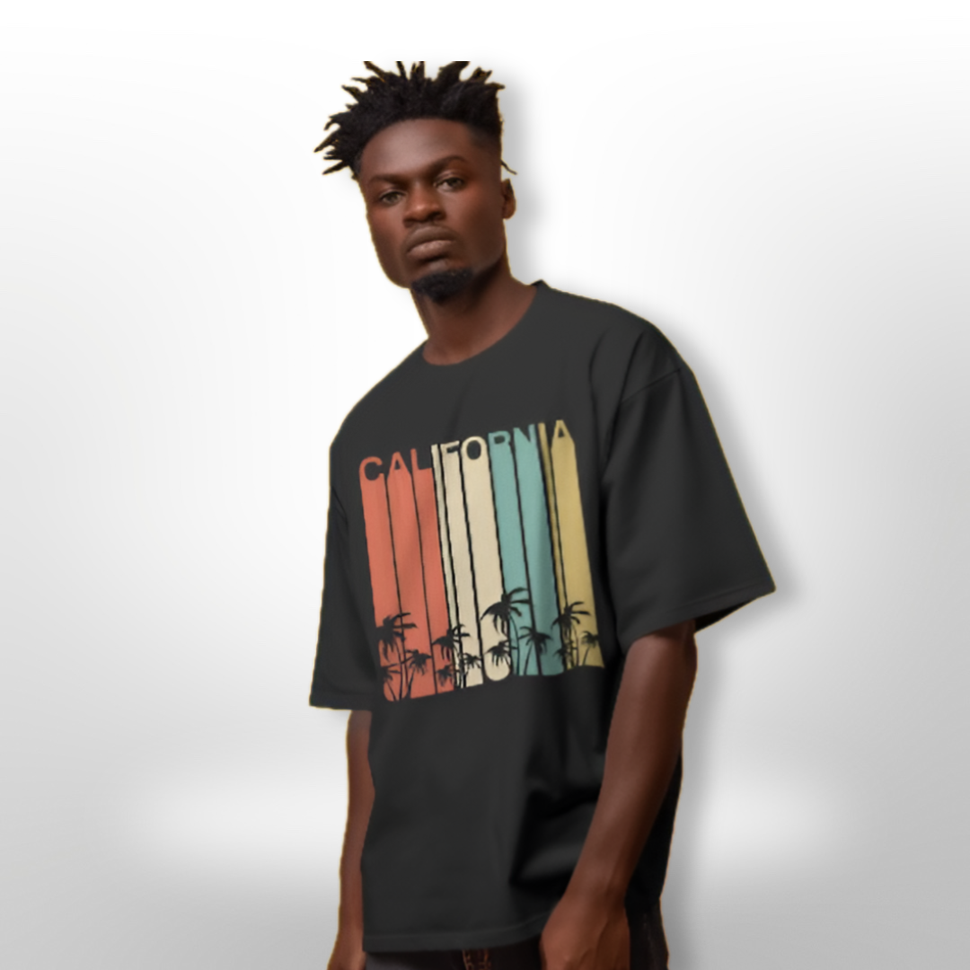 Model wearing the CALIFORNIA design oversized T-shirt at a beach setting, styled with swim shorts for a summer look.